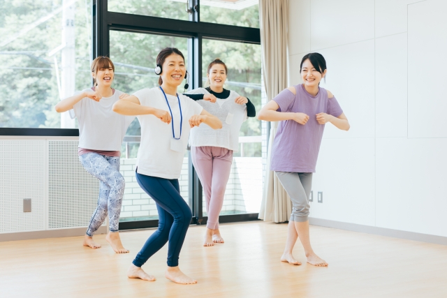 明るいスタジオで、インストラクターと一緒に笑顔で踊る女性たち。